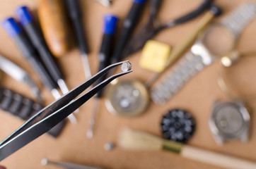 Naklejka premium Watchmaker holding tweezers and little watch battery against lots of professional tools for repairing