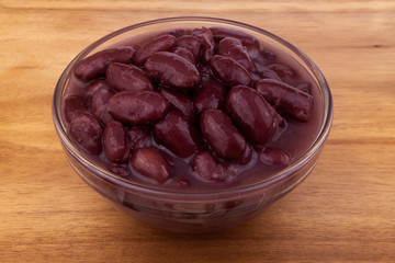 Baked red kidney beans in glass bowl on wooden background