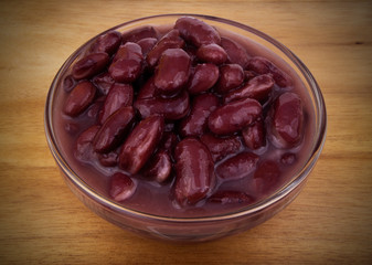 Baked red kidney beans in glass bowl on wooden background