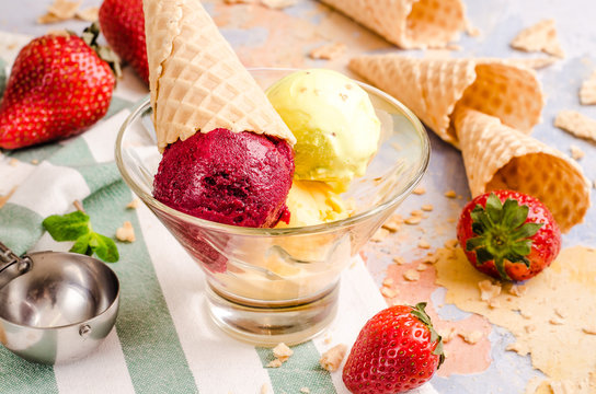 Delicious strawberry ice creams in wafer cones on multi colored background with berries, waffle cup. Homemade healthy summer food, vacation concept.