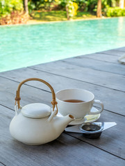 Afternoon tea with white kettle and cup side of pool with natural light