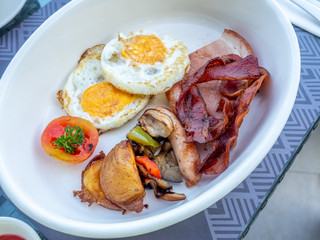 Full meat set of American breakfast with fried eggs, bacon, pork, potato and tomato in white bowl