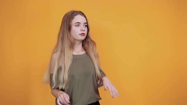 Caucasian attractive girl over orange wall making unimportant gesture stop, looking directly wearing pastel shirt