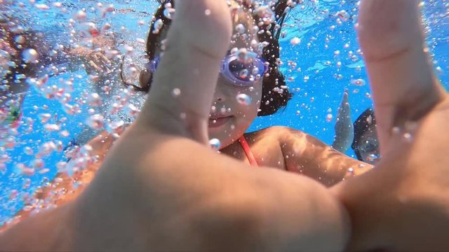 Underwater view of having fun group of children jumping and diving into swimming pool at pool party in summer sunny day. Happy children. Slow motion. Childhood, friendship, vacation concept