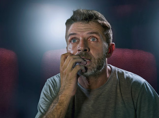 emotional portrait of stressed and excited man at film theater watching cinema thriller or horror...