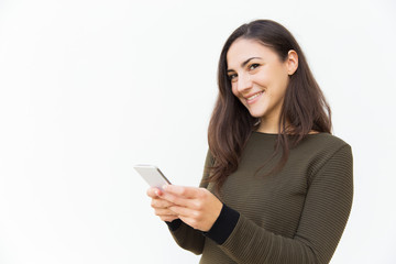 Fototapeta premium Smiling satisfied cellphone user texting message. Young woman in casual with mobile phone standing isolated over white background. Communication concept