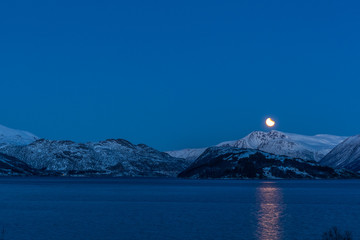 the lunar eclipse during blou hours above mountains lofoten norway. long shutter speed