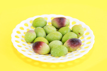 natural green and brown olives in a decorative plate on a yellow background