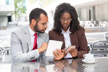 Confident colleagues comparing information from digital devices. Focused coworkers looking at smartphone. Technology concept