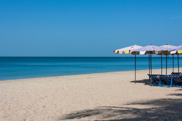 Beautiful breathtaking view of sand beach, turquoise sea, and blue sky with colorful beach umbrella and beach chair on the beach in a sunny day.