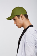 Cropped side photo of a dark-haired man, wearing green baseball cap, black t-shirt and white shirt. He is posing on grey background and looking straight. 