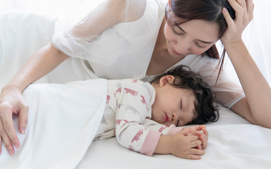 Asian mom and her cute little baby sleeping in bed at home