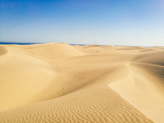 Wide landscape view of vast smooth sand dunes in Maspalomas, Las Palmas of Gran canaria, tropical Canary island in Atlantic ocean, Spain, people in distance
