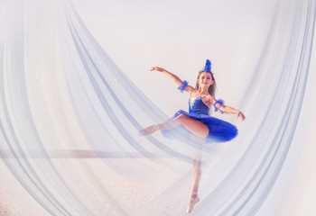 A graceful girl ballerina dances on a snowless landashft among fabrics flying in the air.