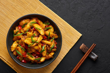 Baby Corn Manchurian dry looks like Schezwan Baby Corn in black bowl at dark slate background. Baby Corn Manchurian - is indo chinese cuisine dish with deep fried corn, bell peppers, sauce and onion.