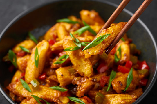 Baby Corn Manchurian dry looks like Schezwan Baby Corn in black bowl at dark slate background. Baby Corn Manchurian - is indo chinese cuisine dish with deep fried corn, bell peppers, sauce and onion.