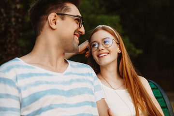 Fototapeta premium Close up of a charming young couple having fun laughing while sitting on a bench and looking to each other.