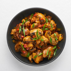 Mushrooms Manchurian dry in black bowl isolated at white background. Mushroom Manchurian - is indo chinese cuisine dish with deep fried mushrooms, bell peppers, sauce and onion.