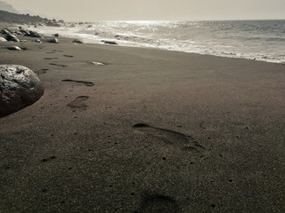 Footprints in black sand on beach Playa de Guayedra in Las Palmas on Gran Canaria volcanic island, Spain, Atlantic ocean, volcanic rocks, coastline, summer, travel adventure, low point of view shot