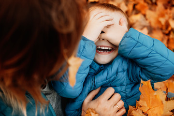 Close up of a happy little kid laughing while hiding his face playing with his mother while mother...