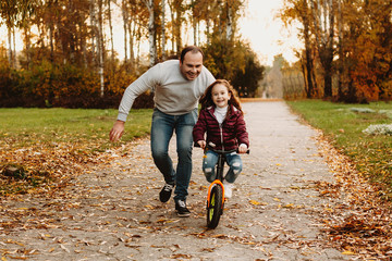 Cute little girl learning how to ride a bicycle in the park outdoor with her father.