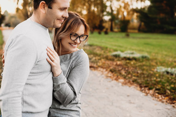Fototapeta premium Portrait of a beautiful young mother embracing her husband while looking at their kids that playing outdoor in the park.