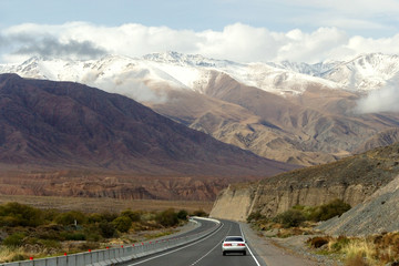 Highway with a car on a background of high mountains, some of which are covered with snow, Kyrgyzstan