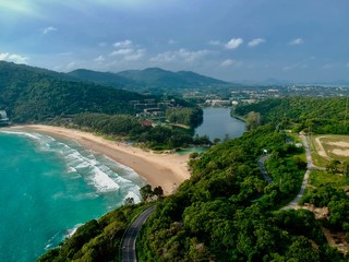 Panorama drone aerial view electricity windmill overlooking Naiharn beach phuket Thailand turquoise blue waters white golden sandy beach lush green mountains 