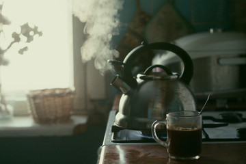  Kitchen. A metal kettle boils on the stove. A cup of coffee. Window. Brown set.