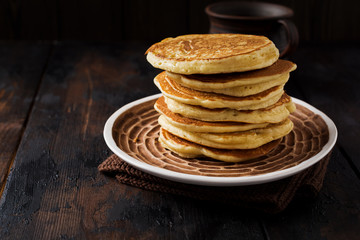 Stack of homemade little pancakes with honey, fresh raspberries and red currants on an old wooden background. Selective focus.