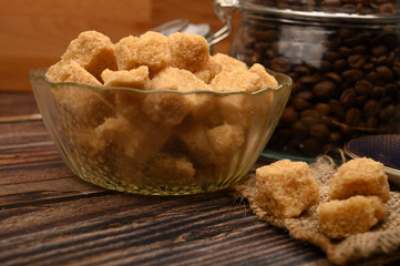 Pieces of brown sugar in a sugar bowl and coffee beans in a glass jar on a wooden background. Close up.