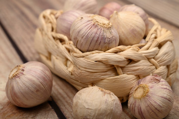 A few heads of young garlic in a wicker basket on a wooden background. Autumn harvest. Modern agriculture. Close up.