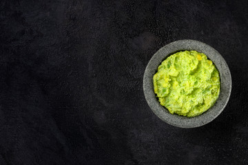 Guacamole avocado dip in a molcajete, typical Mexican stone mortar, top shot on a dark background...