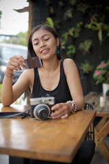Asian girl in a cafe looking on moment photo and hold camera. Beautiful Balinese women in black.