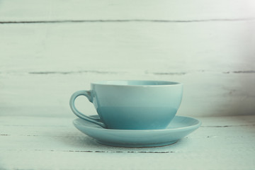 Blue cup and saucer on a white wooden background side view.
