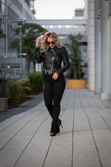 Frau, jung, blond ,schön, modisch, modebewusst und schlank geht im Herbst mit Lederjacke und engen...