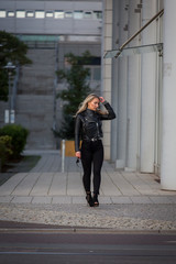 Frau, jung, blond ,sch&ouml;n, modisch, modebewusst und schlank geht im Herbst mit Lederjacke und engen Jeans und Pumps Hackenschuhe durch die Stadt