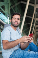 Calm young man sitting on floor at airport. Confident traveler with smartphone looking at camera. Travel concept