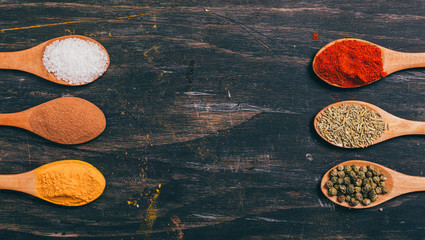Naklejka premium flat lay of colorful spices in spoons on wooden table with copy space.