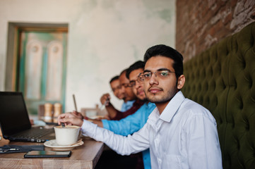 Group of four south asian men's posed at business meeting in cafe. Indians work with laptops together using various gadgets, having conversation and drink coffee.