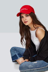 Full length shot of a dark-haired girl, sitting on a floor and wearing red baseball cap with...