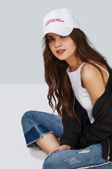 Full length shot of a dark-haired girl, sitting on a floor and wearing white baseball cap with...