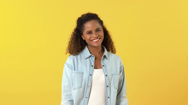 Shy young African American woman smiling and crossing arms against yellow background