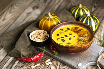 Homemade pumpkin soup with seeds, spices, herbs and croutons on a rustic background copy space