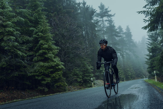 Rennradfahrer im Herbst bei Nebel auf eine Landstra&szlig;e im Wald