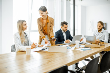 Group of a young office employees dressed casually in the suits having some office work at the meeting table in the bright office