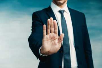 Businessman gesture. Male palm close-up in a gesture of stop. In the background a man in a blue suit with a tie.