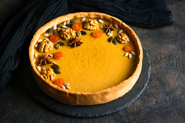 Traditional american homemade holiday pumpkin pie on a dark background with pumpkins.