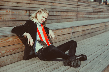 Attractive young man with long blonde hair in a black suit and red tie, rats running around his body. 