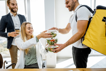 Courier delivering healthy business lunches with thermal bag for the office employees, giving them...